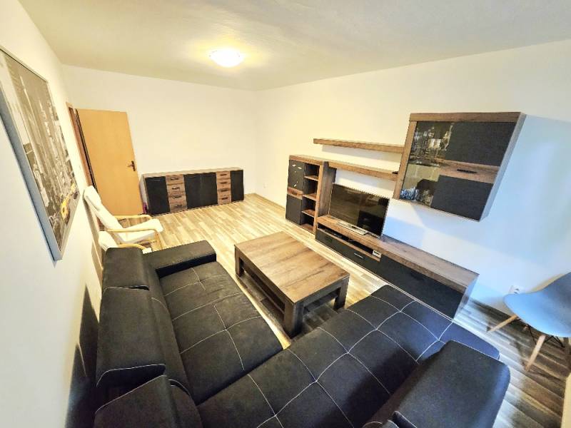 Wohnzimmer in einer 3-Zimmer-Wohnung mit schwarzem Sofa, Möbeln und Holzboden.