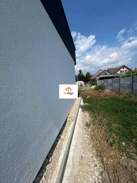Die Wand eines Einfamilienhauses in Žihárec mit angrenzendem Grundstück unter blauem Himmel.