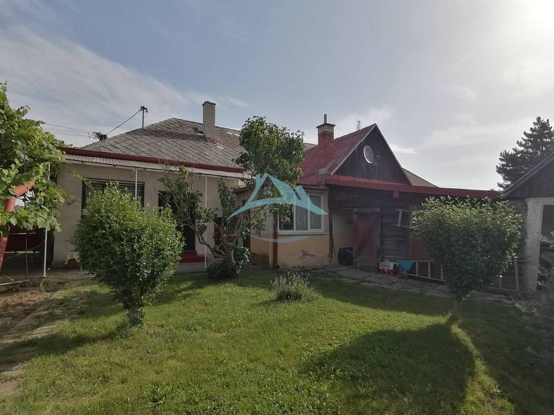 Ein Einfamilienhaus in Hrkovce mit Garten, Sträuchern und einem Holzunterstand.
