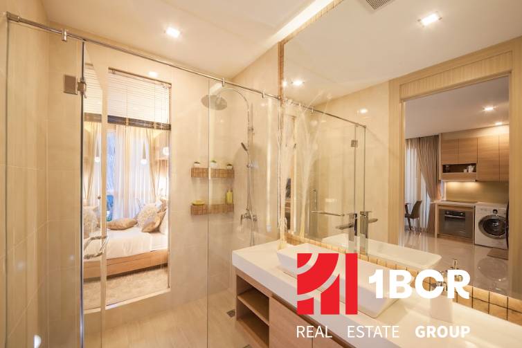 Badezimmer in einer 2-Zimmer-Wohnung mit Duschkabine und Waschbecken, das ins Schlafzimmer führt.