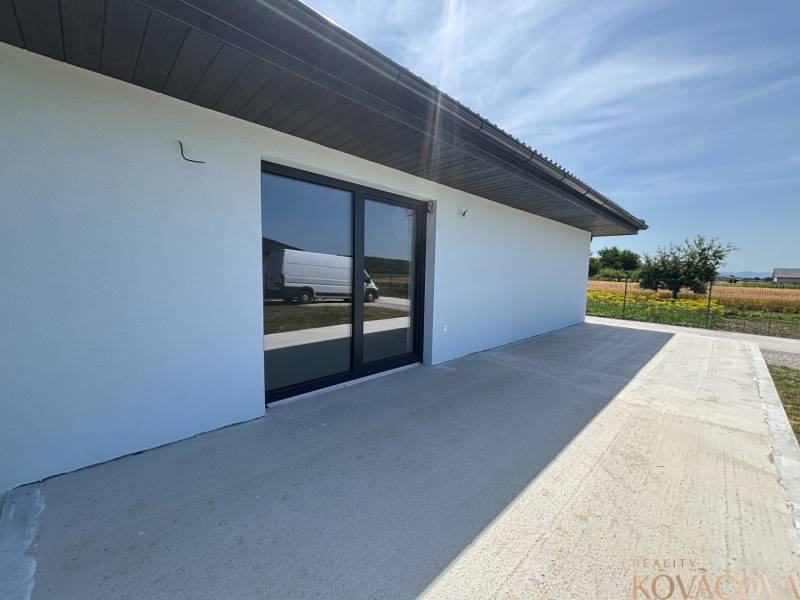 Ein Einfamilienhaus in Podlužany mit einer geräumigen Terrasse und großen Glastüren.
