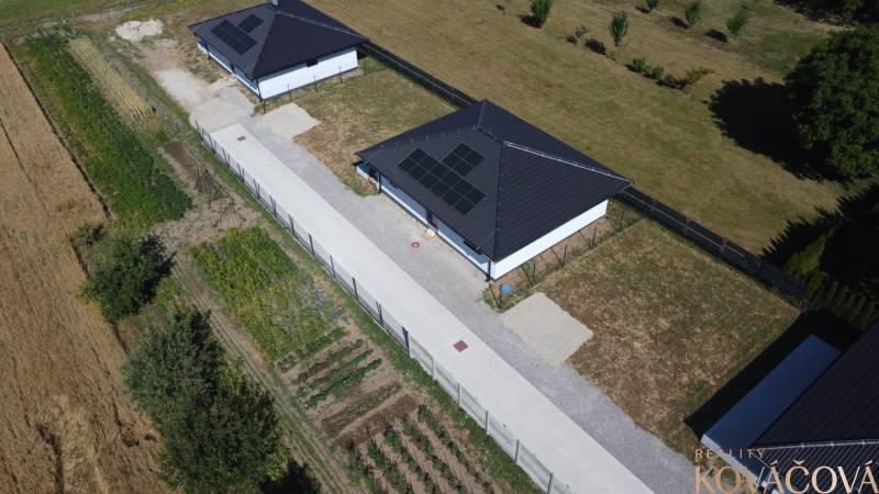Ein Einfamilienhaus in Podlužany mit Photovoltaikmodulen, einem Garten und umliegenden Feldern.