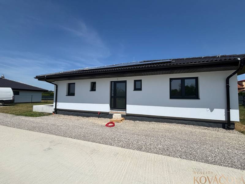 Ein Einfamilienhaus in Podlužany mit Solarpaneelen und einem Schrägdach auf einem Kiesgrundstück.