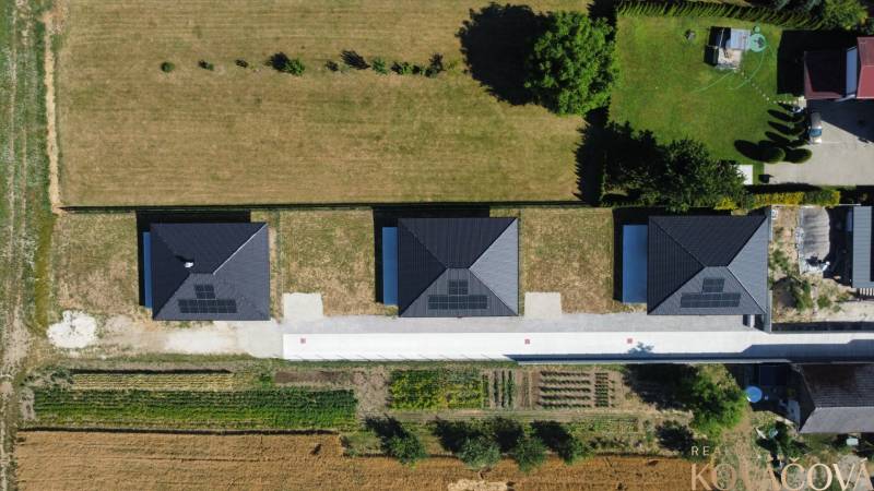 Luftaufnahme von drei Einfamilienhäusern in Podlužany mit Solarpaneelen auf den Dächern.