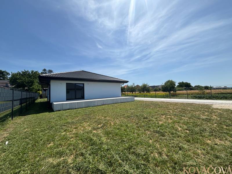Ein Einfamilienhaus in Podlužany mit einem großen Rasen, neben einem Feldweg und einem Zaun.
