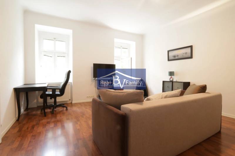 Wohnzimmer in einer Zweizimmerwohnung mit Sofa, Schreibtisch und Fernseher.