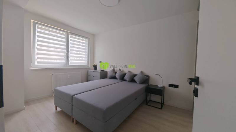 Schlafzimmer in einer Einzimmerwohnung mit Ehebett, Nachttischen und einem Fenster mit Rollläden.