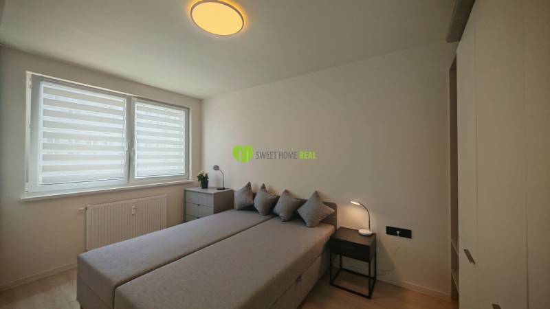 Schlafzimmer mit Bett, Schrank und Fenstern in einer Einzimmerwohnung, neutrale Farben.