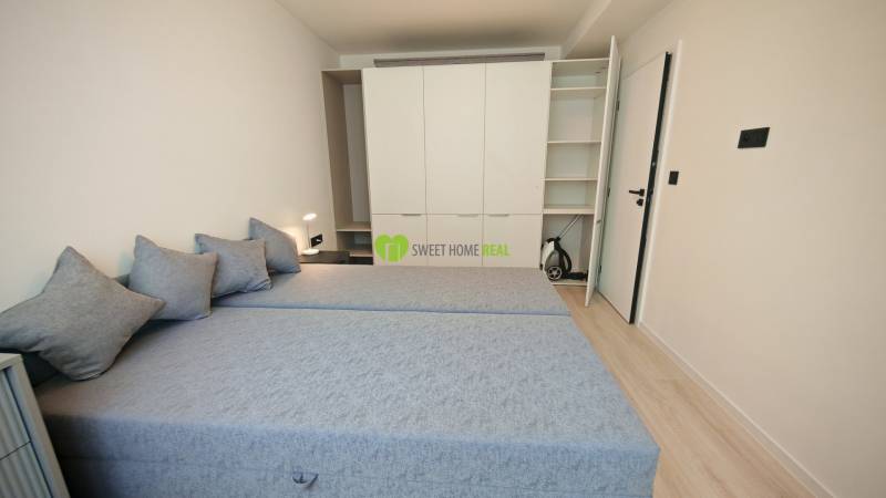 Schlafzimmer in einer Einzimmerwohnung mit zwei Betten, Einbauschrank und Nachttischlampe.