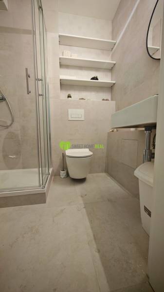 Badezimmer in einer Einzimmerwohnung mit Toilette, Duschkabine und Wandregalen.