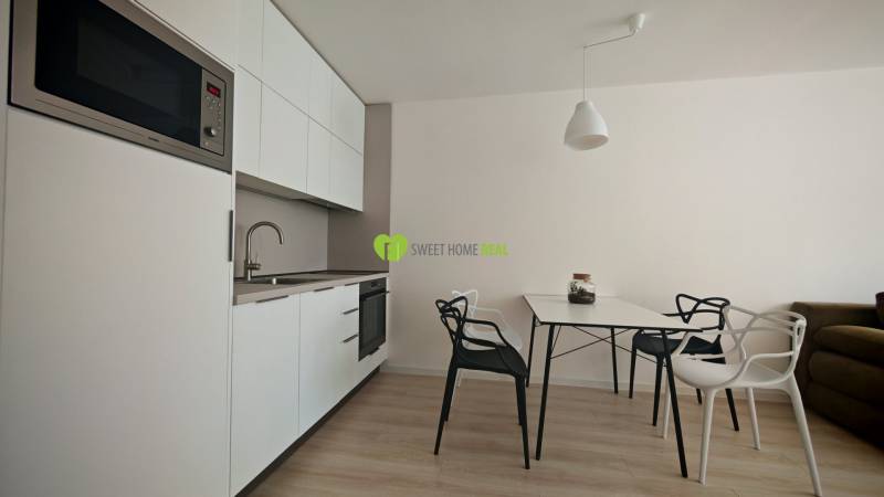 Küchenecke in einer Einzimmerwohnung mit weißen Schränken und Esstisch.