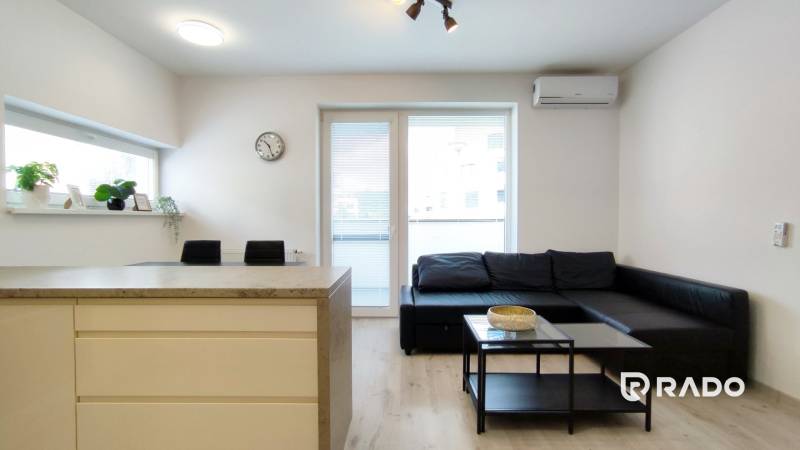 Wohnzimmer in einer 2-Zimmer-Wohnung mit Sofa, Tisch und Zugang zum Balkon.