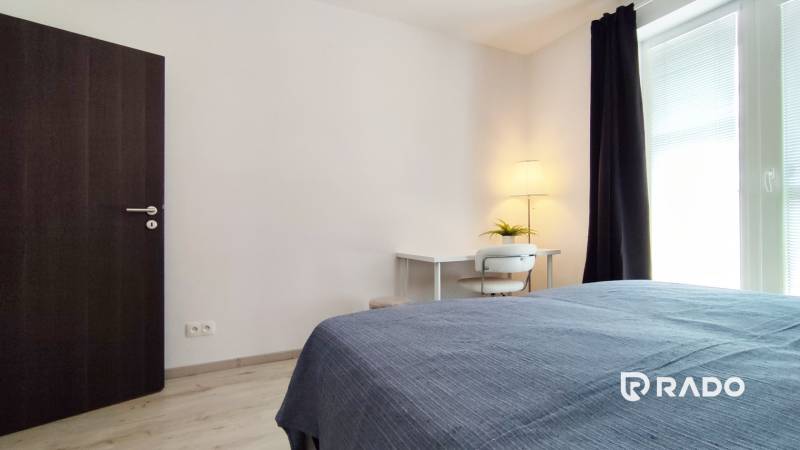 Schlafzimmer in einer Zweizimmerwohnung mit Schreibtisch, Lampe und Bett.