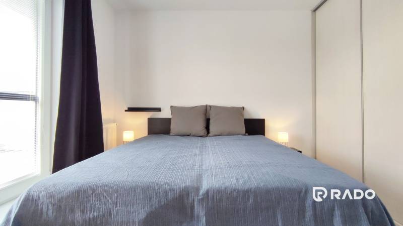 Schlafzimmer in einer 2-Zimmer-Wohnung mit einem großen Bett, Fenster mit dunklen Vorhängen.