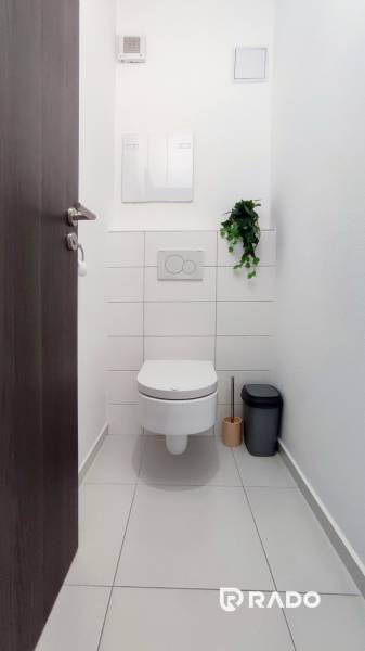 Toilette in einer 2-Zimmer-Wohnung mit weißen Fliesen und Reinigungszubehör.