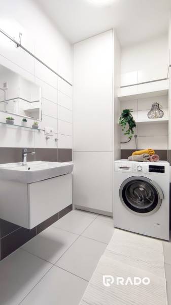 Badezimmer in einer 2-Zimmer-Wohnung mit Waschmaschine, Waschbecken und Regalen mit Dekorationen.