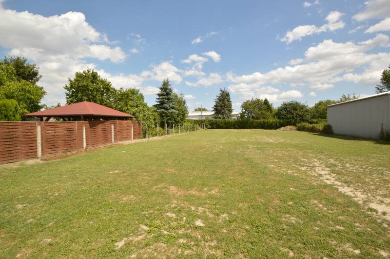 Garten bei einem Einfamilienhaus in Rajka, Rasen, Pavillon, Zaun, Bäume unter blauem Himmel.
