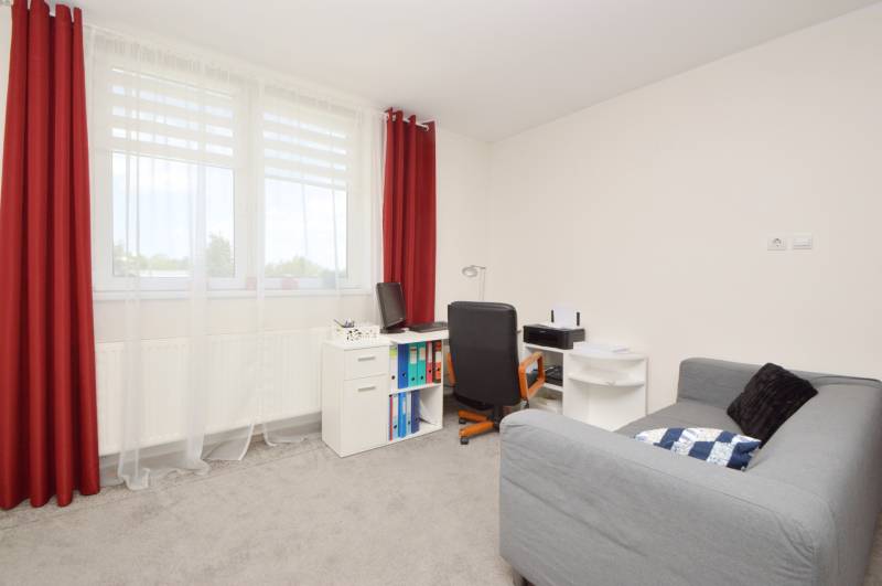 Ein Zimmer in einem Einfamilienhaus mit Sitzgelegenheit, Schreibtisch und roten Vorhängen.