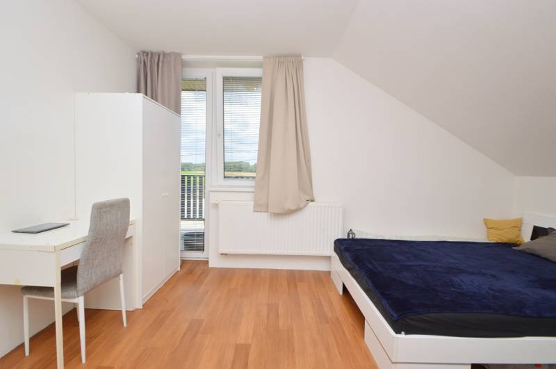 Helles Zimmer in einem Einfamilienhaus mit Bett, Tisch und Schrank.