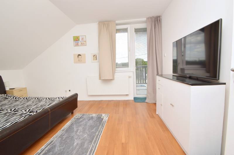 Schlafzimmer in einem Einfamilienhaus mit Bett, Fernseher, Schrank und Zugang zum Balkon.