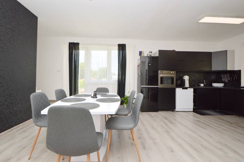 Esszimmer mit Küche in einem Einfamilienhaus mit schwarzen Möbeln und grauen Stühlen.