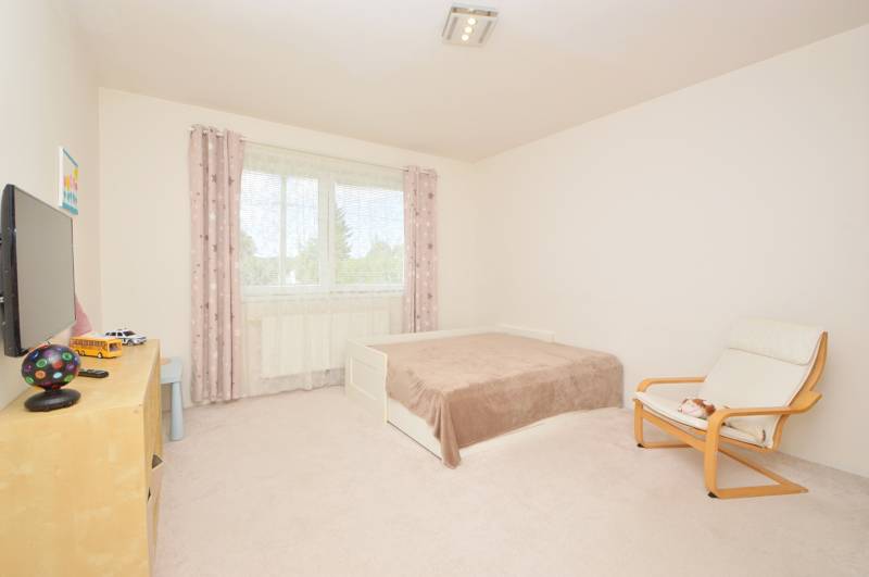 Helles Zimmer mit Bett, Sessel und Fernseher in einem Einfamilienhaus.