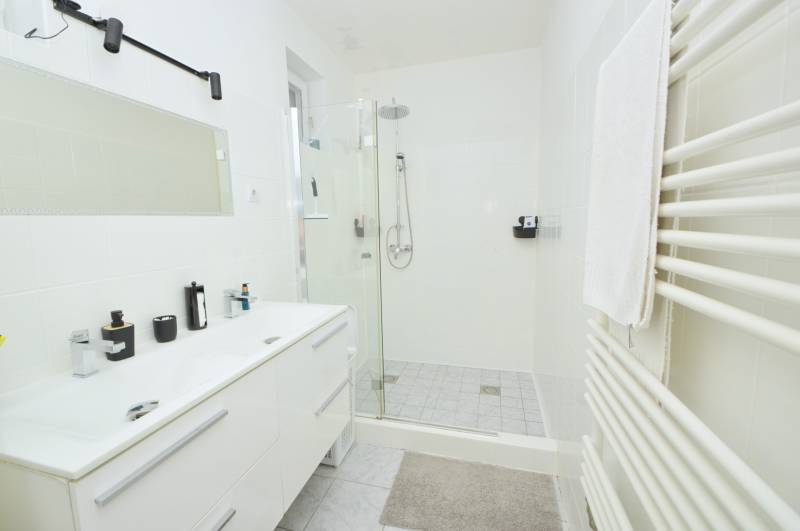 Badezimmer mit weißem Waschtischunterschrank, gläserner Duschkabine und Handtuchheizkörper.