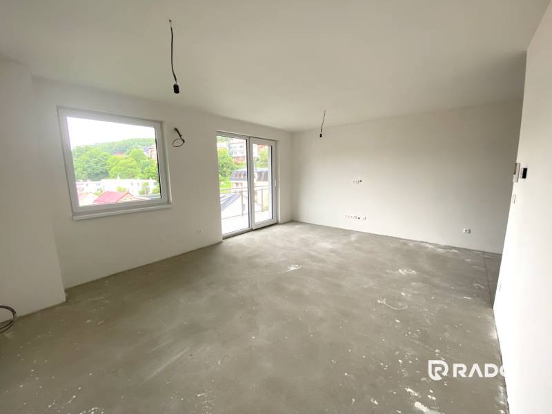 Geräumiges Zimmer einer 2-Zimmer-Wohnung mit großen Fenstern und Betonboden.