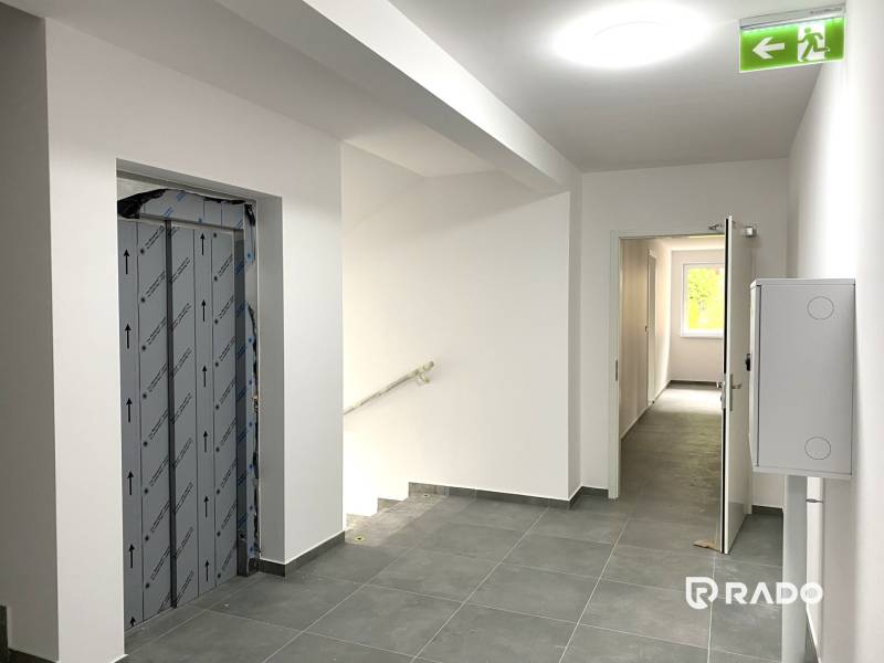 Der Flur mit Treppe, Aufzug und offenen Türen zu einer 2-Zimmer-Wohnung.