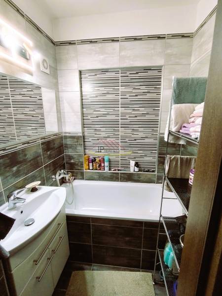 Badezimmer in einer 2-Zimmer-Wohnung mit Badewanne, Waschbecken und einem Regal mit Handtüchern.