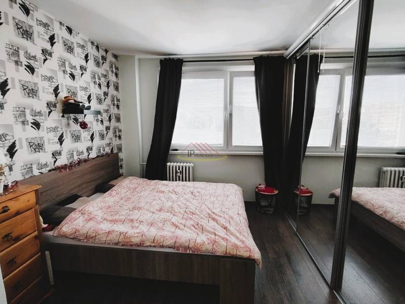 Schlafzimmer in einer 2-Zimmer-Wohnung mit großem Fenster, Schiebetüren mit Spiegeln und dekorativer Wand.