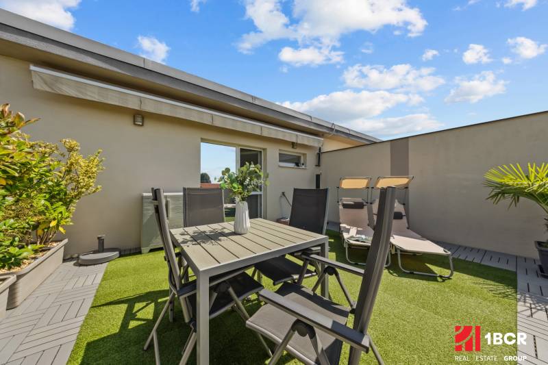 Die Terrasse einer 4-Zimmer-Wohnung mit Tisch und Stühlen, umgeben von Pflanzen und Liegestühlen.