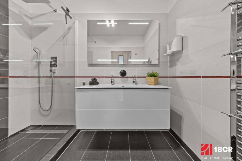Badezimmer mit Waschbecken, Duschkabine und Spiegel in einer 4-Zimmer-Wohnung.