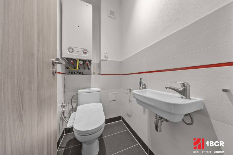 Badezimmer in einer 4-Zimmer-Wohnung mit Toilette, Waschbecken und einem Boiler an der Wand.