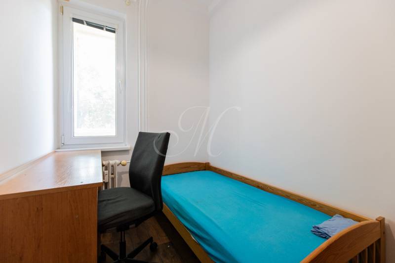 Einfaches Zimmer in einer 4-Zimmer-Wohnung mit Bett, Tisch und schwarzem Sessel.
