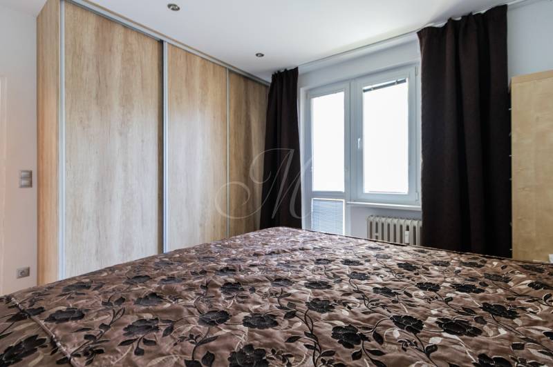 Schlafzimmer mit Einbauschrank, gepolstertem Überwurf und Fenster in einer Vierzimmerwohnung.