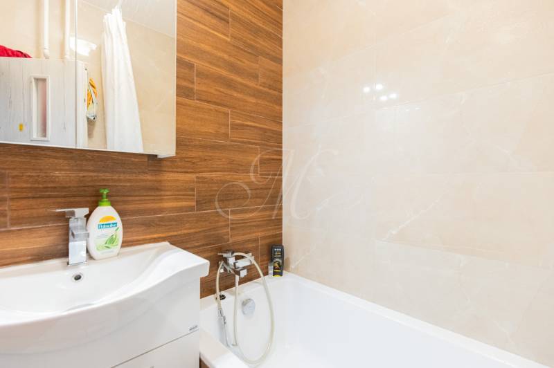 Ein Badezimmer in einer 4-Zimmer-Wohnung mit einem Spiegel, einer Badewanne und einer Holzverkleidung an der Wand.