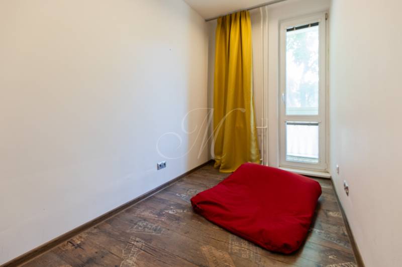 Ein Zimmer mit gelben Vorhängen, einer roten Matratze und Holzboden in einer Vierzimmerwohnung.