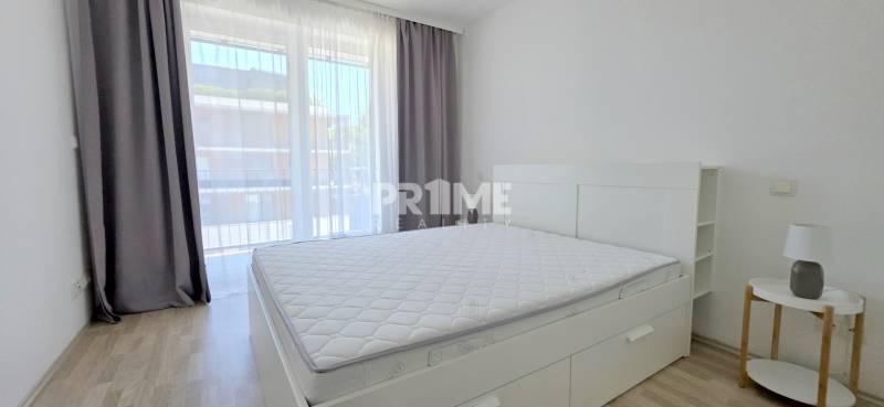 Helles Schlafzimmer mit großem Fenster, Bett und Nachttisch in einer 2-Zimmer-Wohnung.