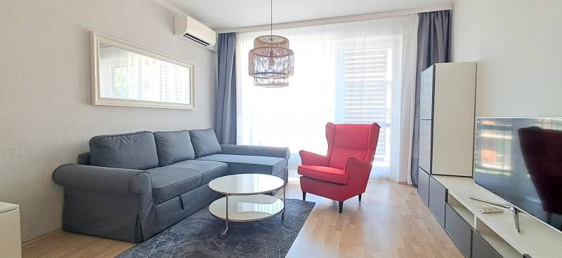 Wohnzimmer mit einem bequemen Sofa, einem roten Sessel und einem Fernseher in einer 2-Zimmer-Wohnung.
