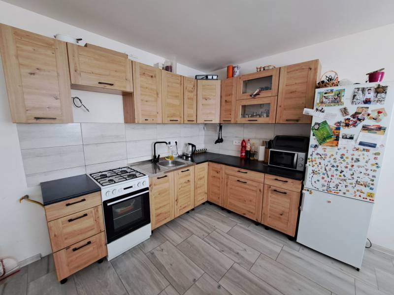 Eine Küche in einem Einfamilienhaus mit hellen Holzschränken, einem weißen Kühlschrank und einem Elektroherd.