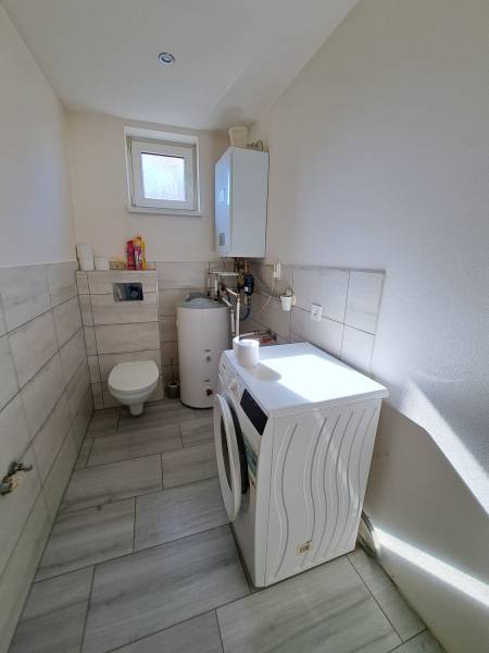 Waschküche in einem Einfamilienhaus mit Waschmaschine, Boiler und Toilette.