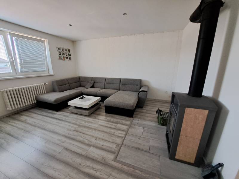 Wohnzimmer mit Ecksofa, Kaminofen und Tisch in einem Einfamilienhaus.