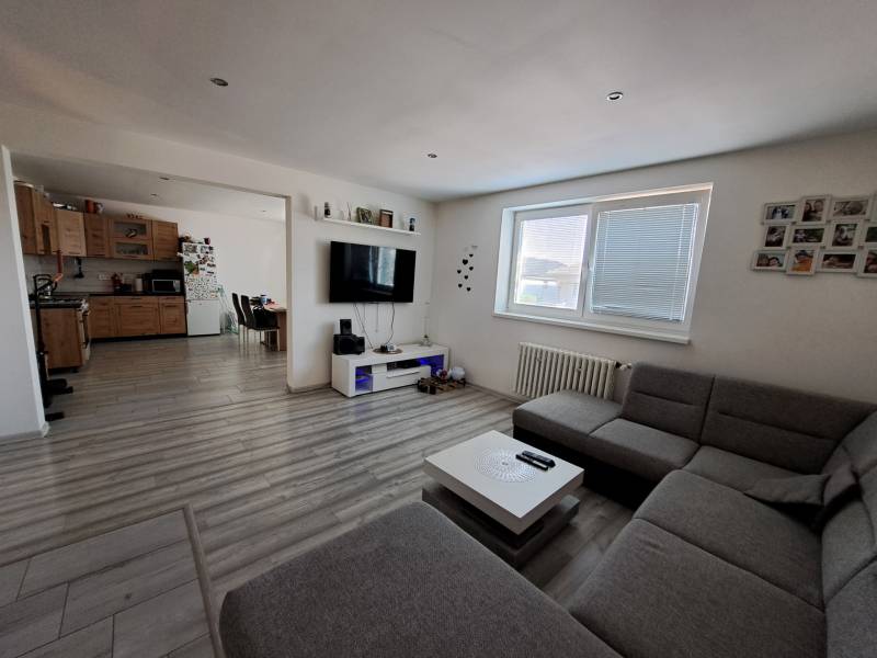 Wohnzimmer mit Küche in einem Einfamilienhaus mit Sofa, Fernseher und Holzschränken.