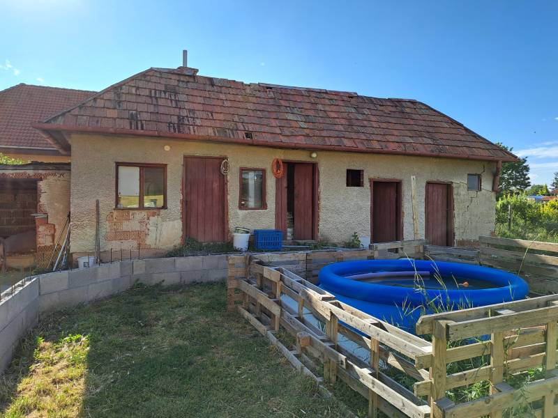 Ein Einfamilienhaus in Kmeťovo mit Anbau, aufblasbarem Pool und einfachem Holzzaun.