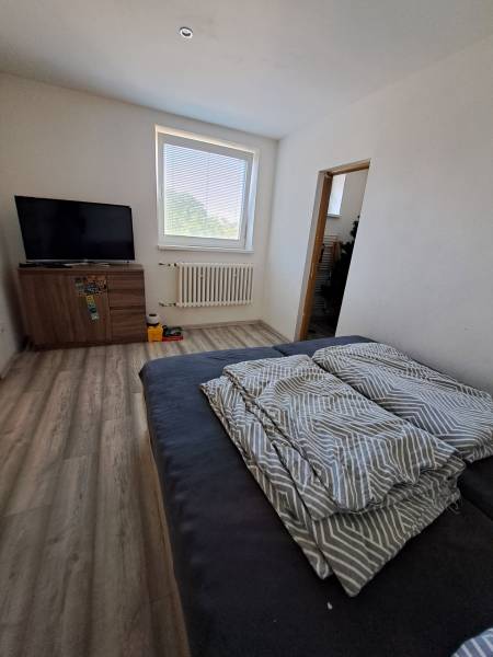 Ein Zimmer in einem Einfamilienhaus mit einem Fernseher, einem Sofa und einem Fenster, das natürliches Licht hereinlässt.