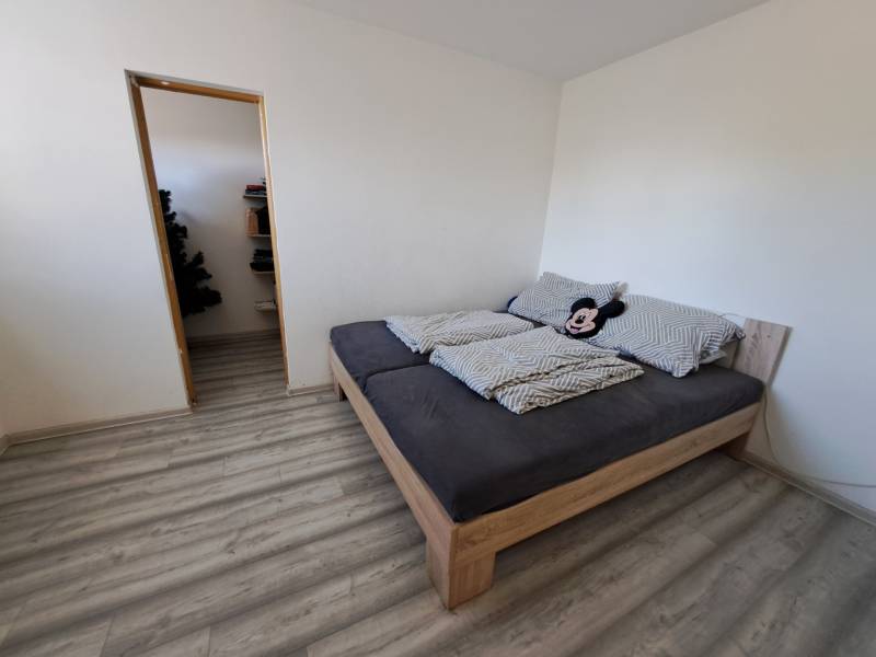Schlafzimmer eines Einfamilienhauses mit Bett, weinrotem Boden und Eingang zur Speisekammer.