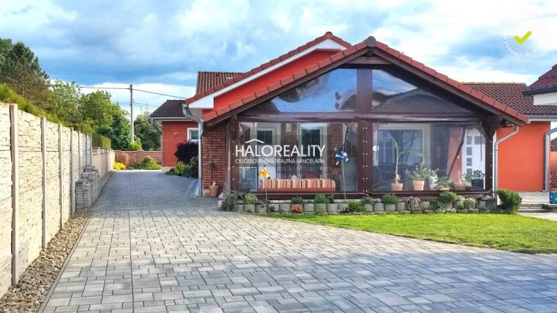 Ein Einfamilienhaus in Kalinovo mit einer gepflasterten Zufahrt und einer verglasten Veranda.