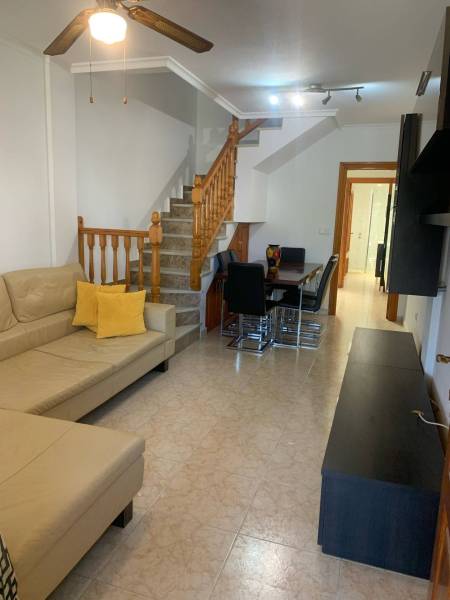 Wohnzimmer eines Einfamilienhauses mit beigem Sofa, Esstisch und Holztreppe.