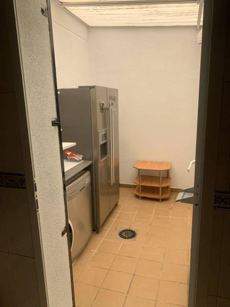 Waschküche in einem Einfamilienhaus mit Kühlschrank, Waschmaschine und kleinem Tisch auf gefliestem Boden.